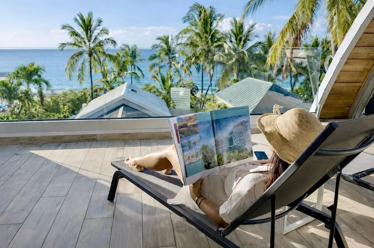 Une cliente lit sur un transat du rooftop, face à l'océan et aux cocotiers